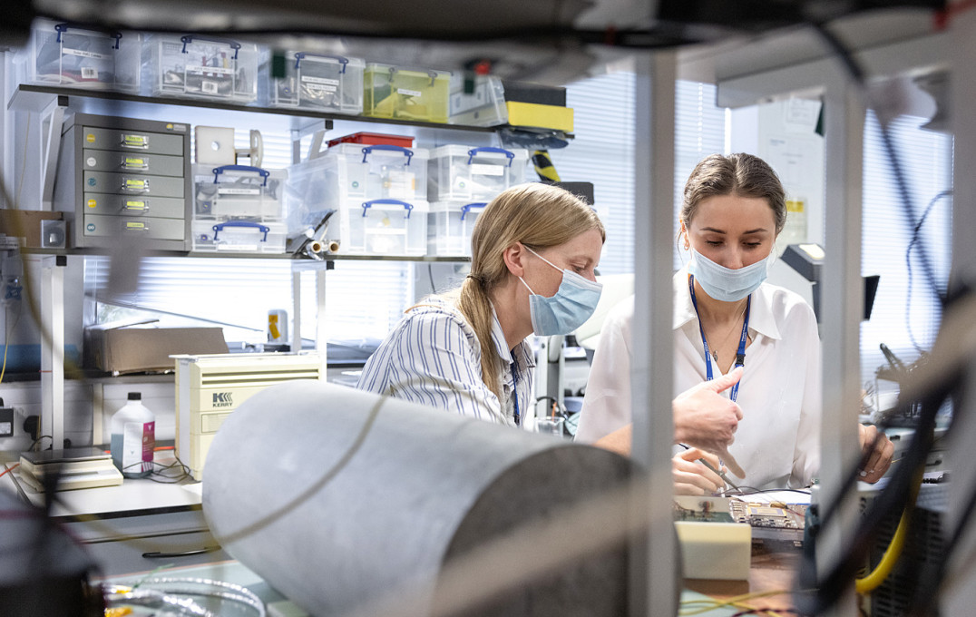 Two women in masks working on some electronics on a lab bench