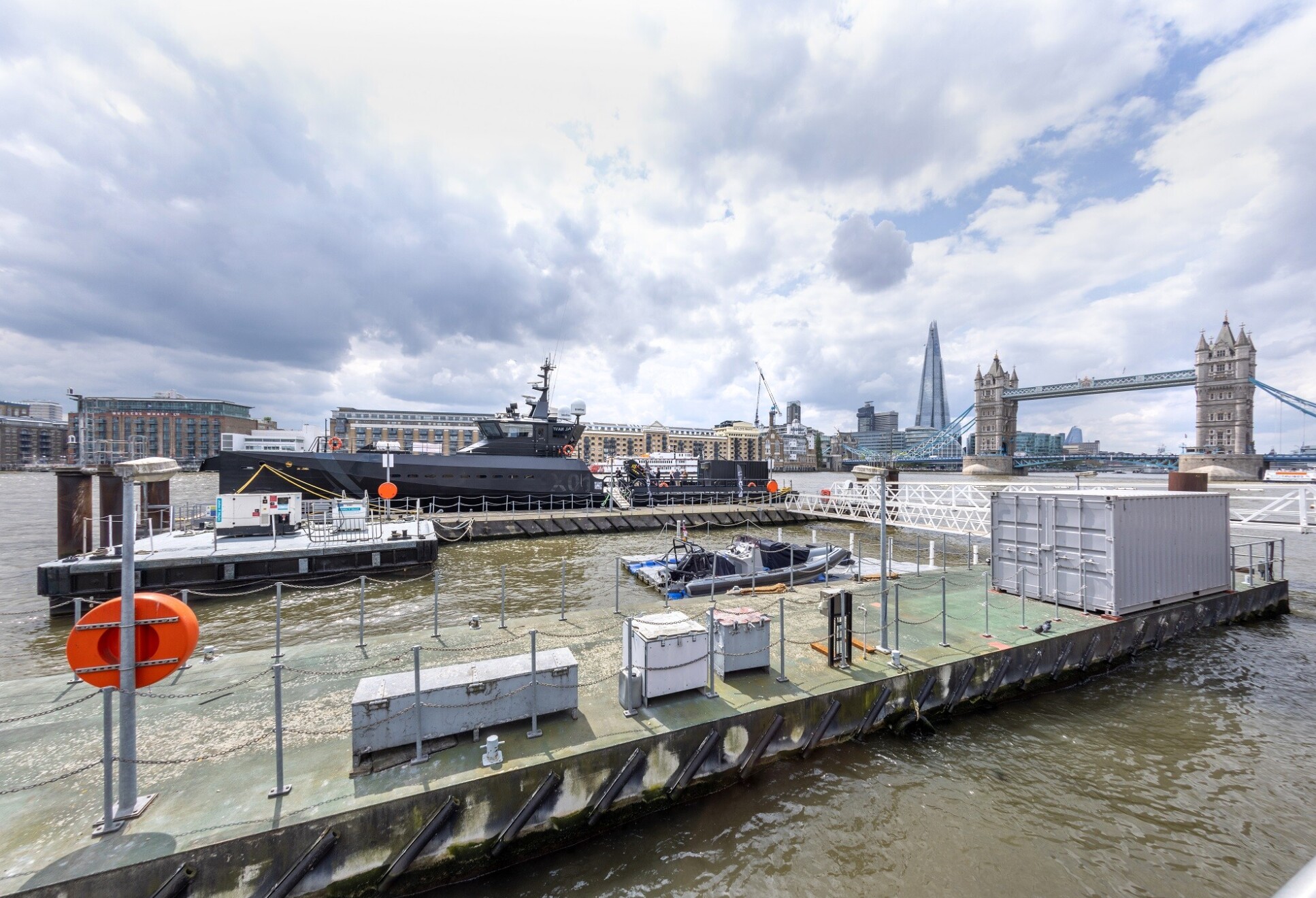 A black ship with Tower Bridge and The Shard in the background, plus pontoons in the foreground