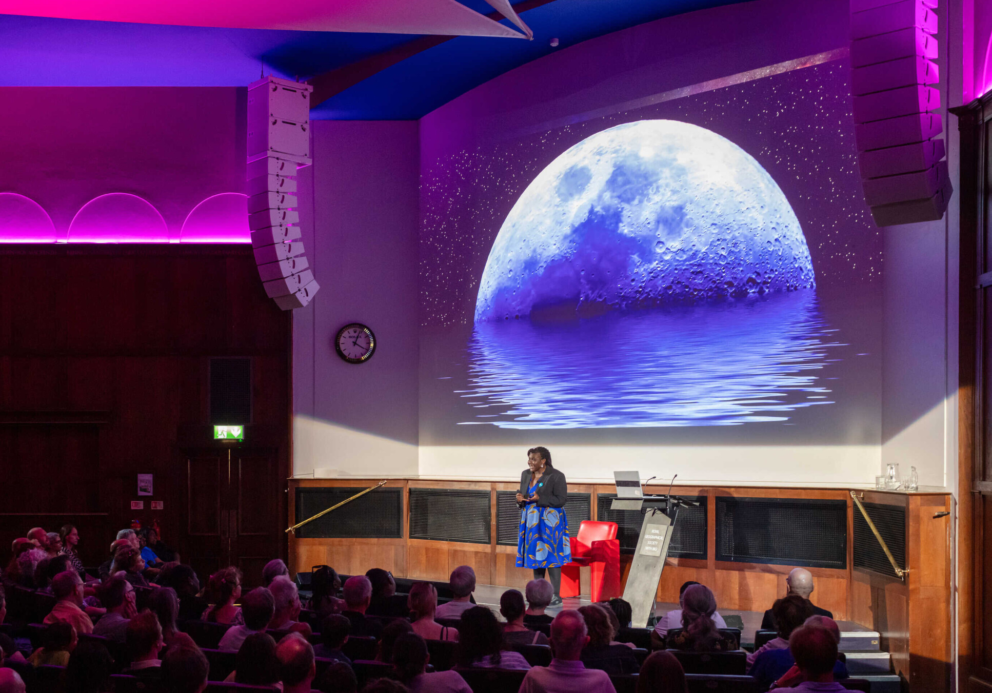 Dr Maggie Aderin Pocock giving a talk with large photo of the moon projected on a screen