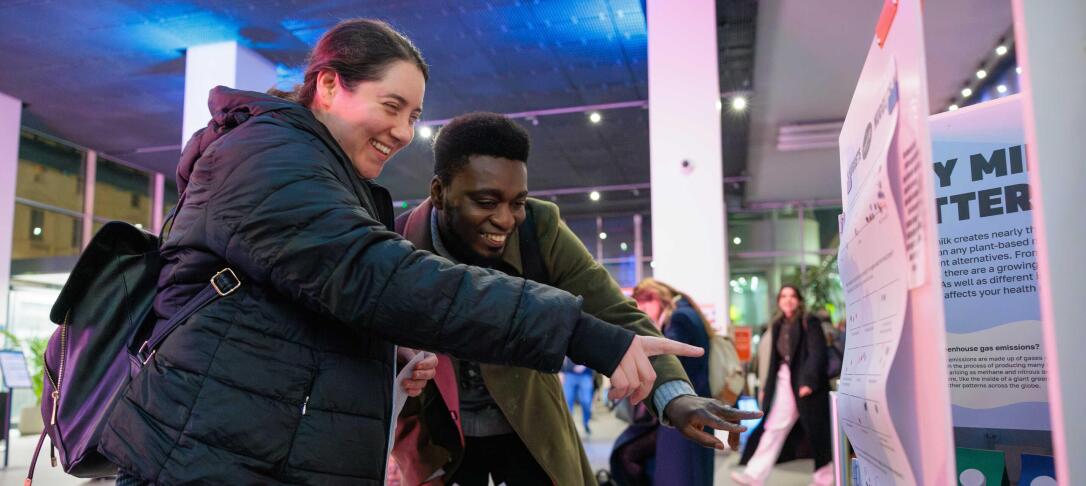 Two Imperial Lates visitors smiling and pointing at something at an exhibit