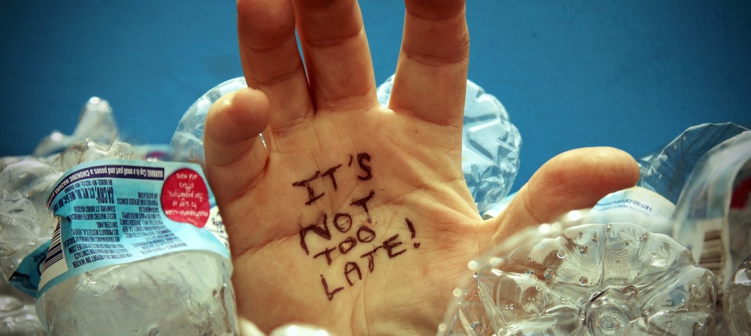 Photograph of plastic waste bottles, with palm of hand with writing on it 'it's not too late'