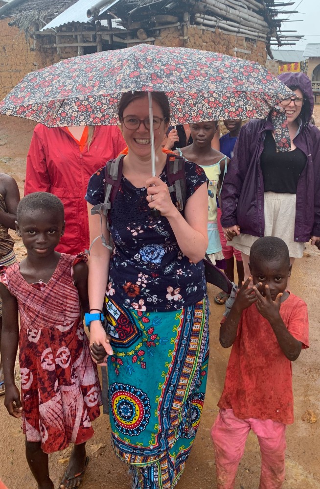 Dr Wainwright standing in the rain with Ugandan children, holding an umbrella