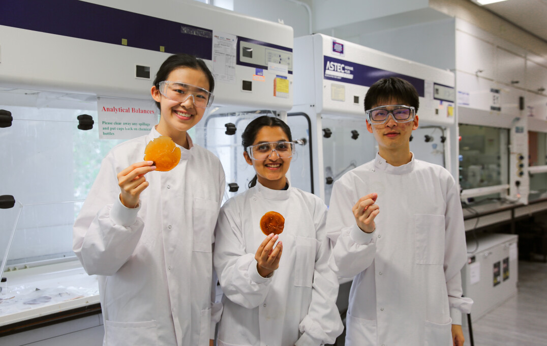 Three students in lab coats showing waste masterial