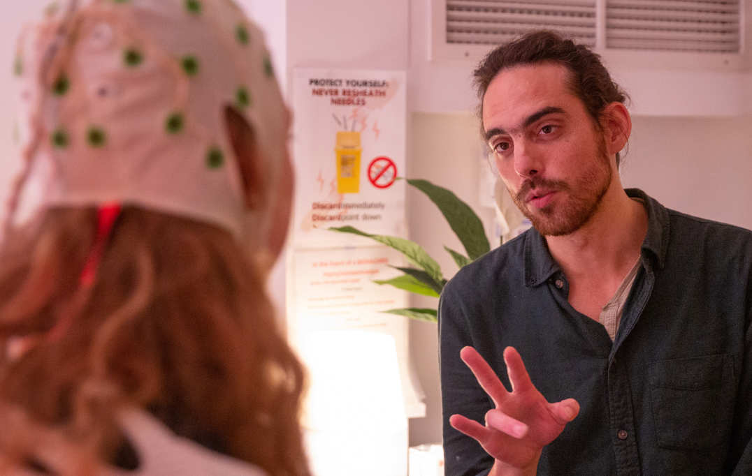 Lead researcher Chris Timmermann talks to a volunteer wearing an EEG cap to measure their brain activity