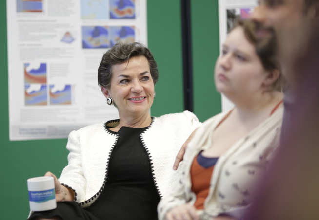 Woman in white jacket leans back to look at room of students