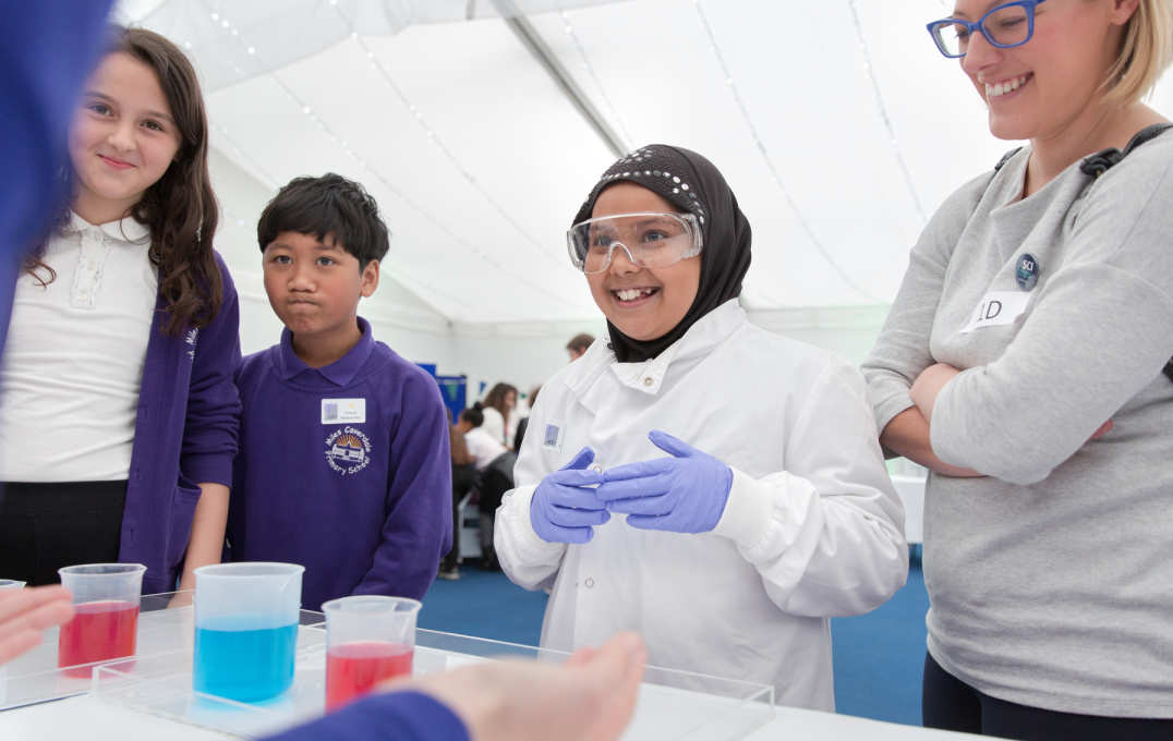 A young girl wears a lab coat and eye goggles