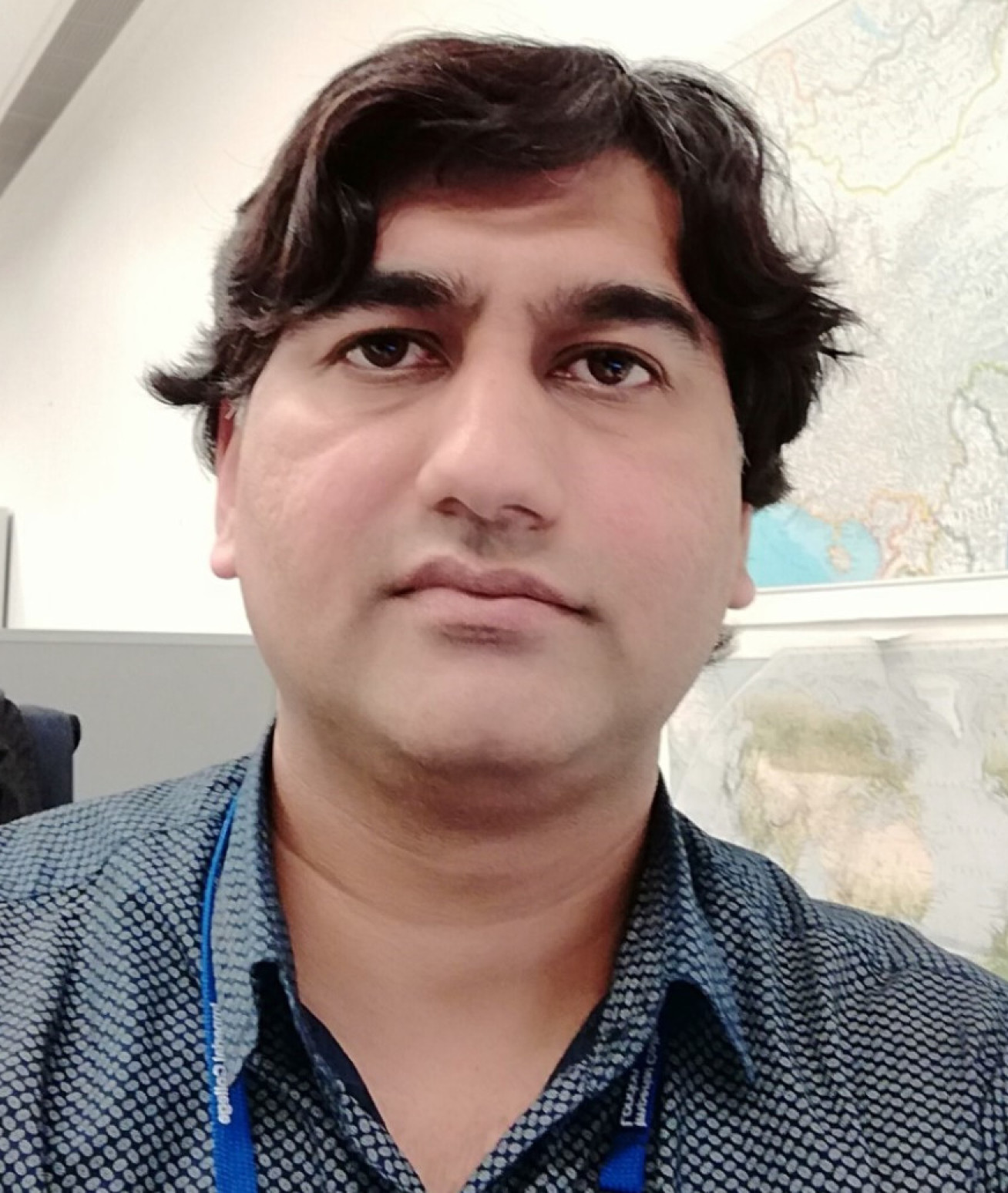 Lead author Dr Abdul Malik inside an office with maps on the wall 