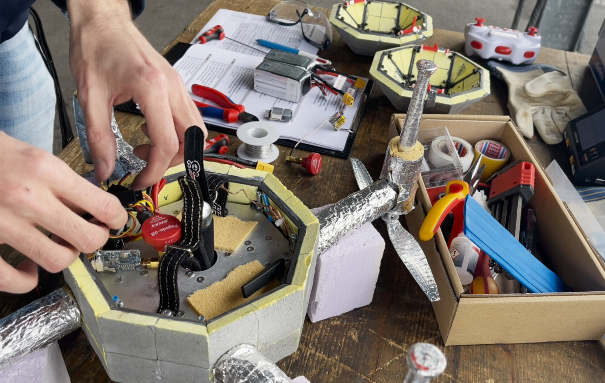 Hands fiddling with wired inside a drone, with a layer of insulating material around the outside