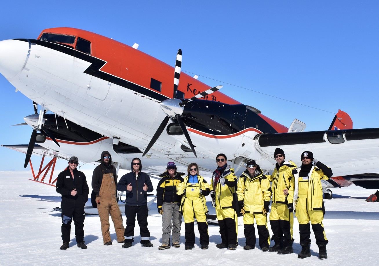 Group of scientists stand in front of an aircraft landed on the snow of Antarctic