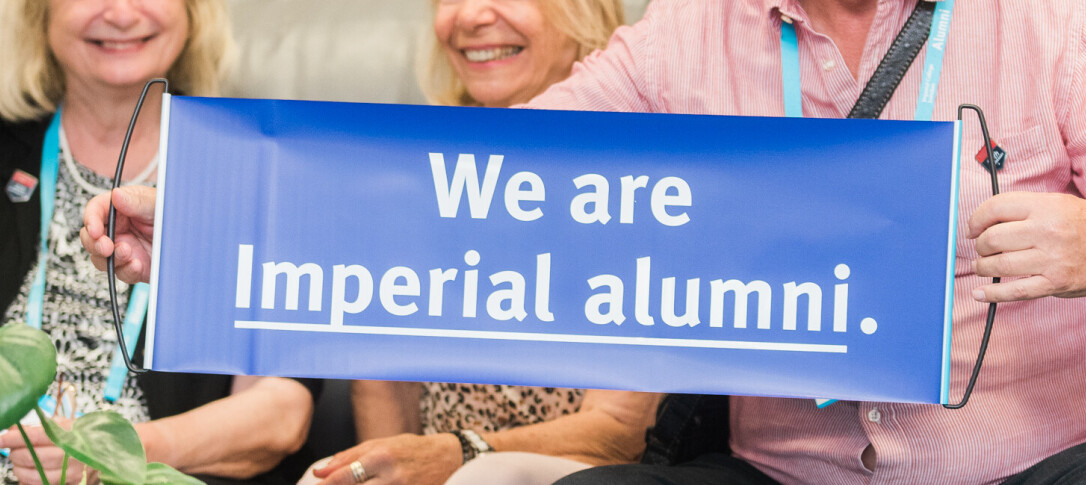A group of three senior alumni, faces not visible, at an event. One holds up a purple pull-out banner that reads 'We are Imperial alumni.' The photo is cropped so that only their hands and part of their upper halves are visible. 