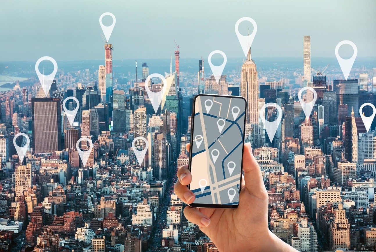 New York city skyline, with someone holding up a smartphone in the foreground, with location markers dotted around the city