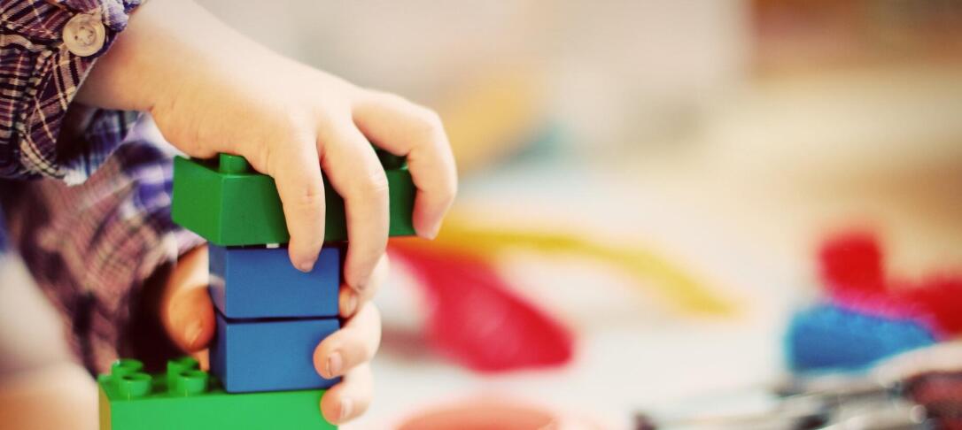 child's hand playing with primary colour plastic bricks