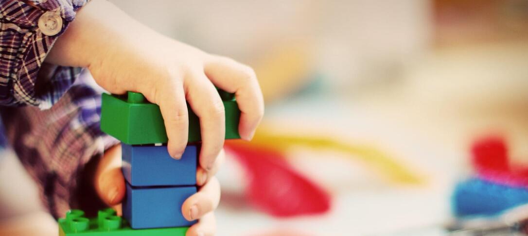 child's hand playing with primary colour plastic bricks