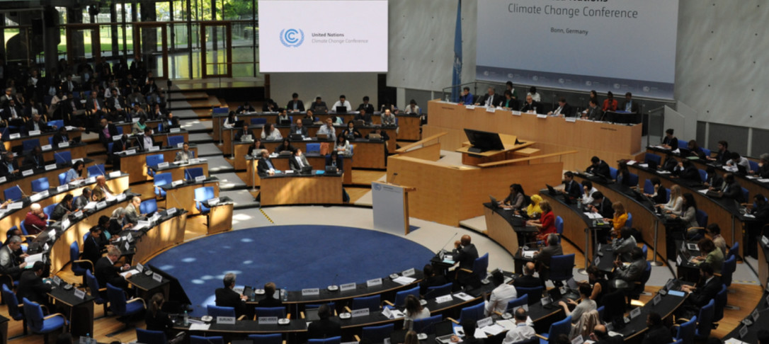 Hall filled with people sitting at desks, a screen reads: United Nations Climate Change Conference, below the UN logo
