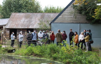 Group of students stands in front of barn and next to pond