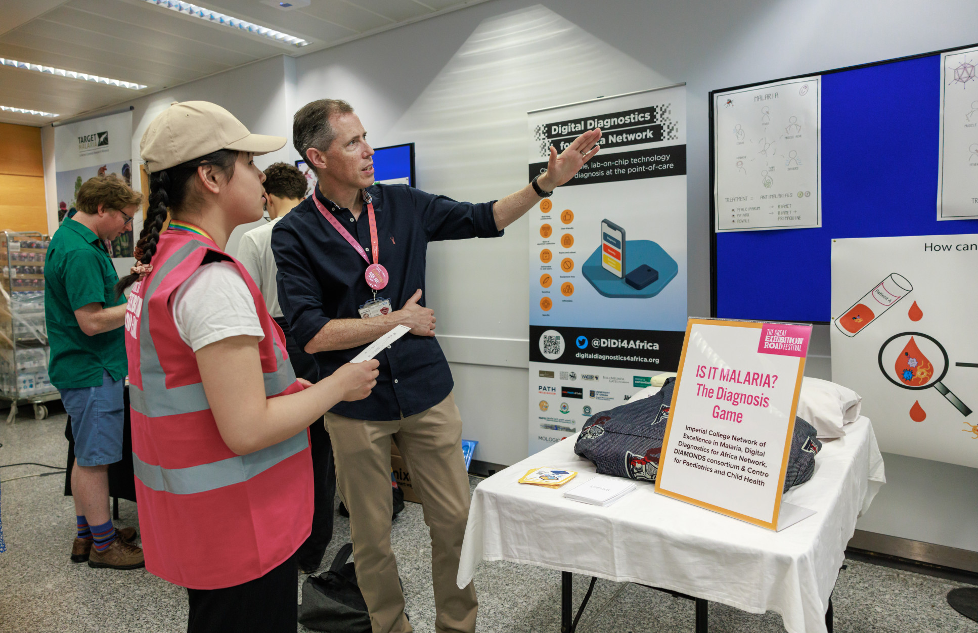 A researcher pointing to posters in conversation with a young attendee