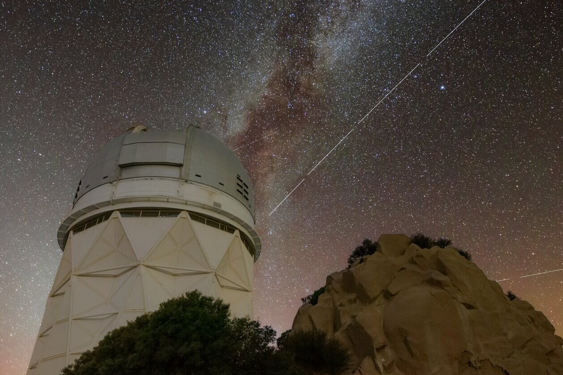 Bright streak across the night sky behind a large telescope