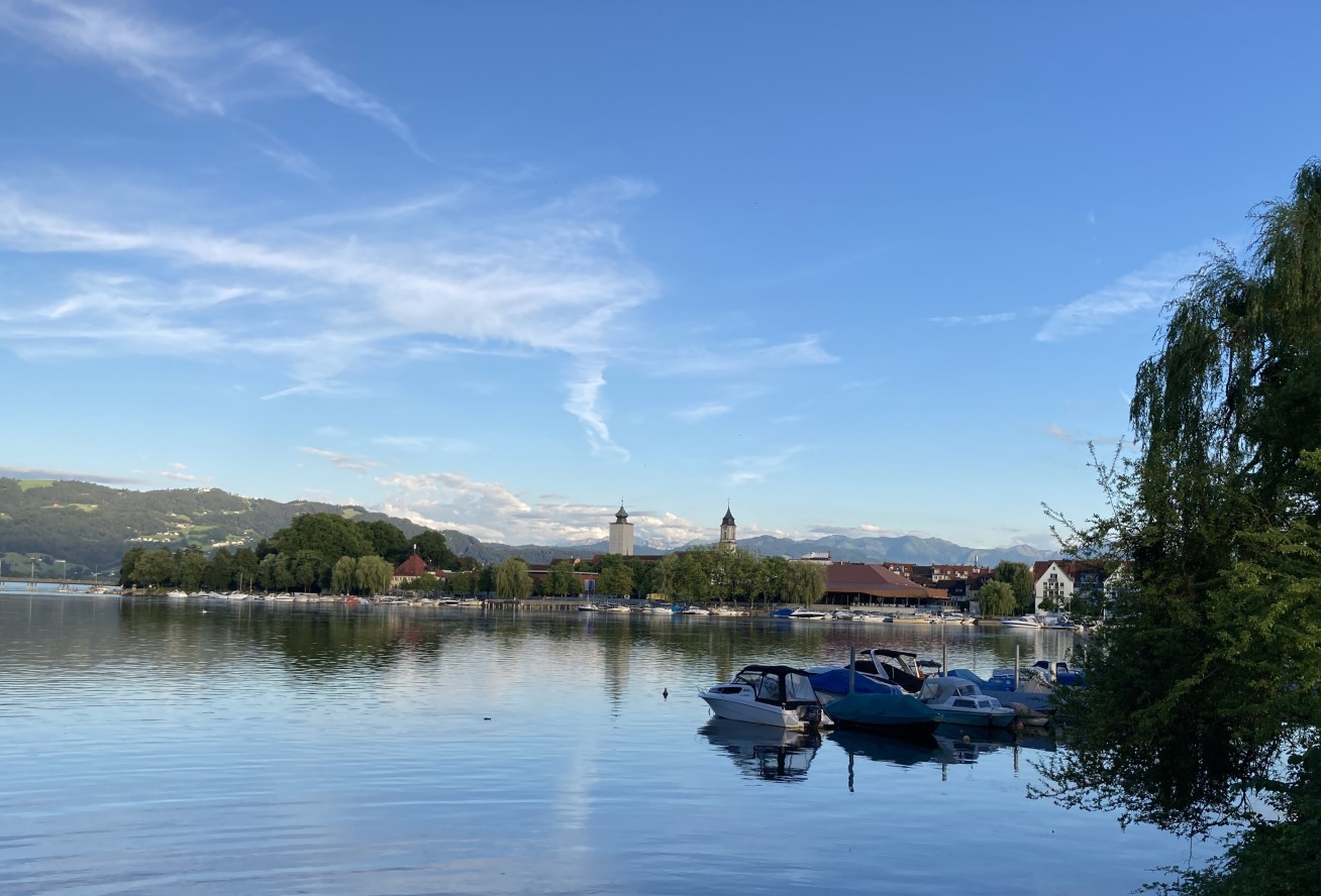 An island with two spires seen from across the water. The sky is blue and there are mountains in the background.