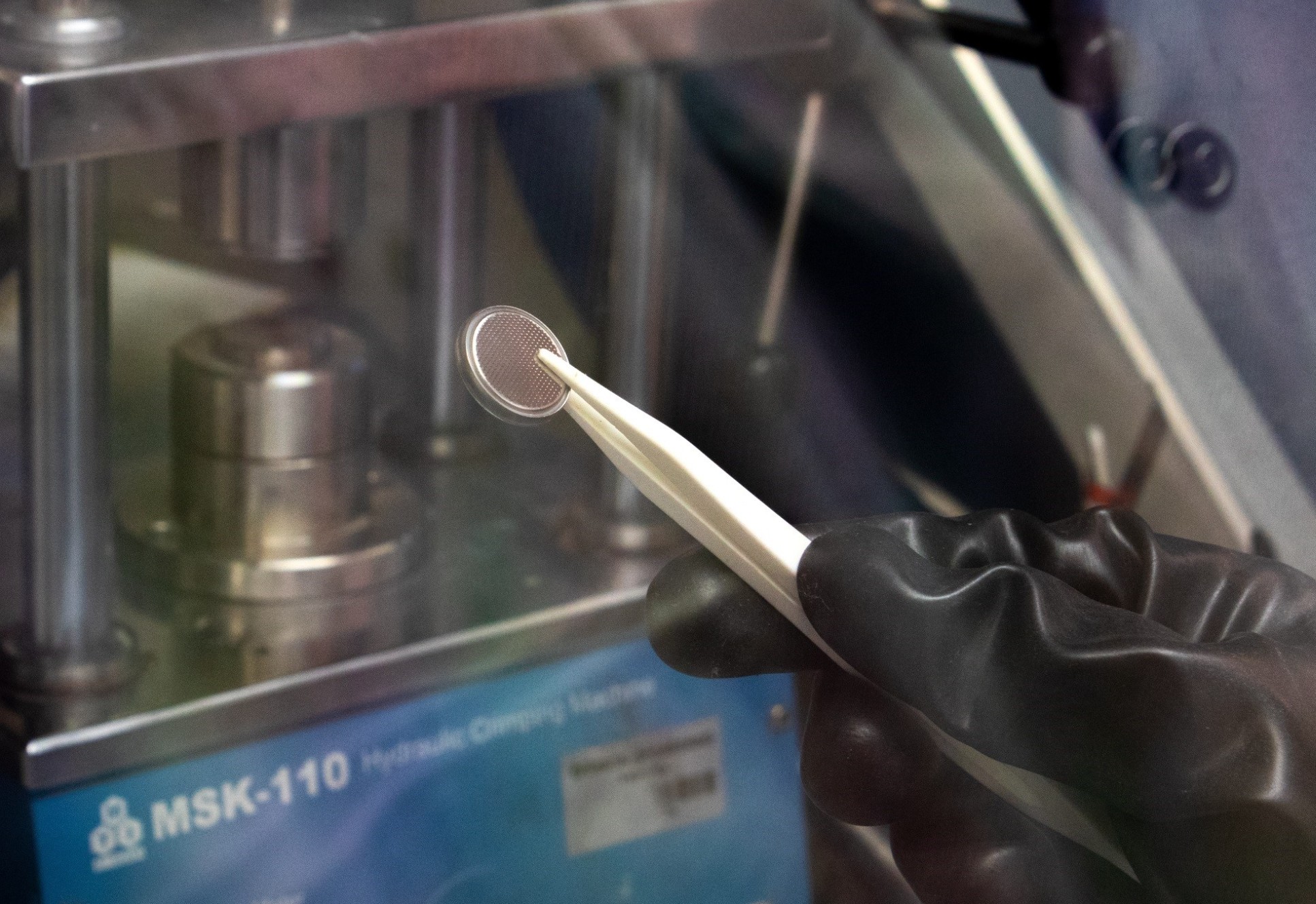 A round silver battery being held with tweezers