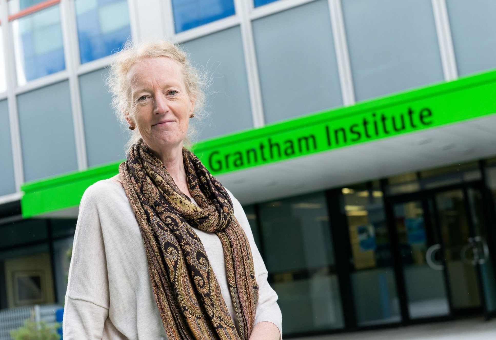 Professor Joanna Haigh a women with blonde hair stands in front of an office sign that reads Grantham Institute. 