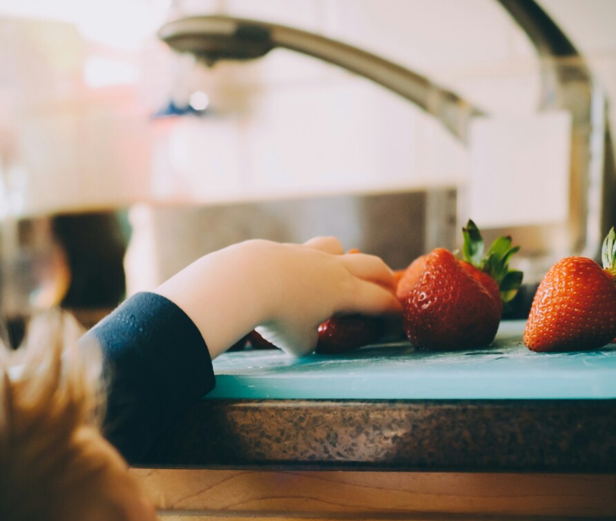 Child reaching for strawberries on kitchen counter