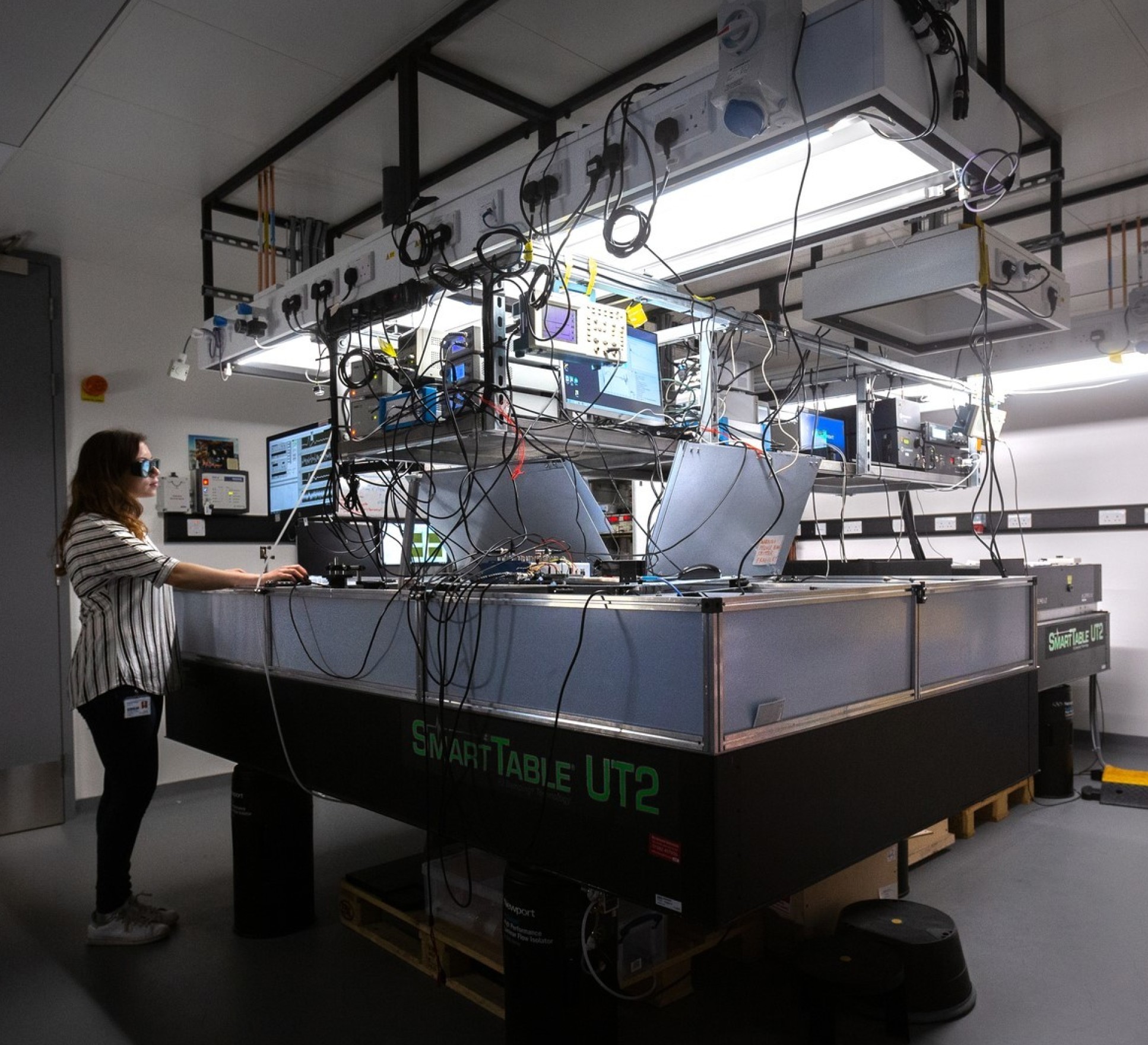 Researcher standing at a computer on a table of laser equipment