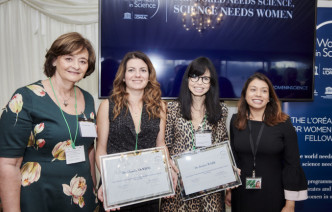 Jess Wade and Claudia Contini in front of a sign that reads 'The world needs science, science needs women'