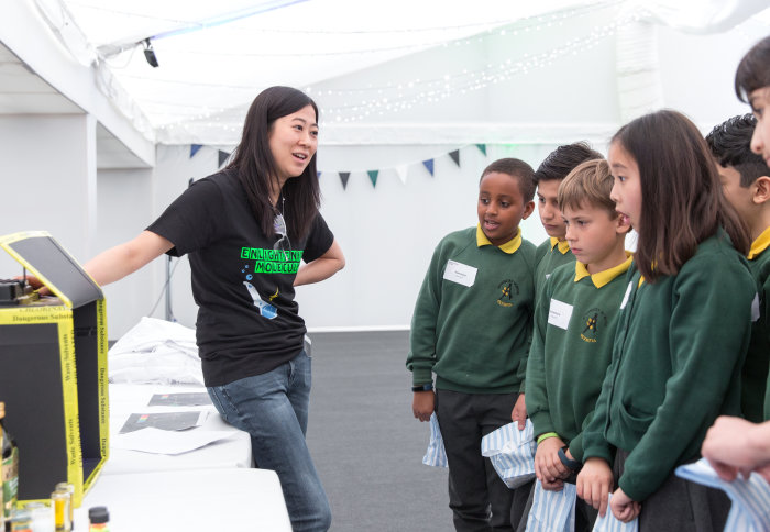 School children watch a display of fluorescent household objects.