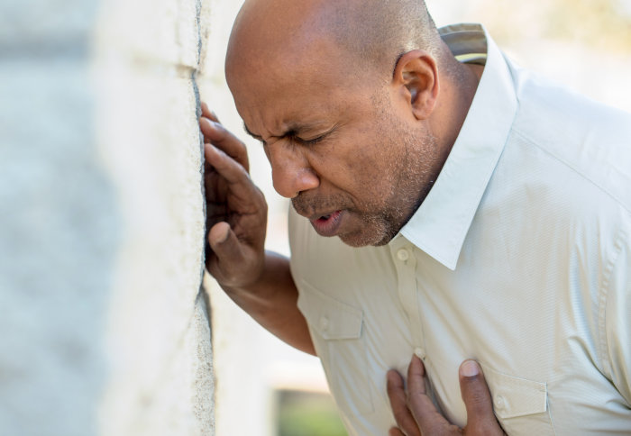 Man clutches chest and leans against wall