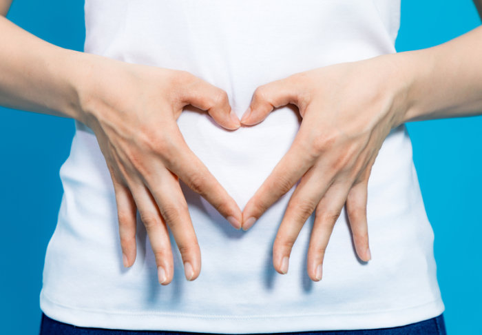 A woman holding her hands over her belly in the shape of a heart