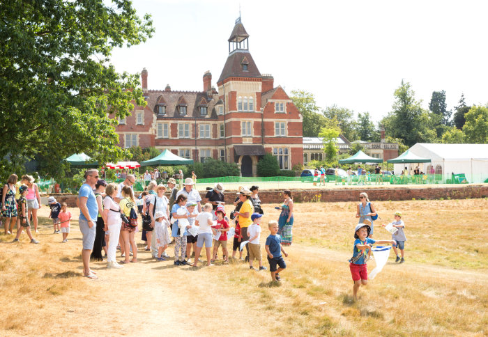 People on a lawn in front of an old red-brick building. A boy holds out a butterfly net.