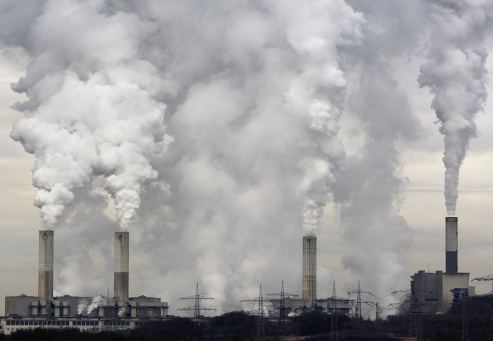 Four factory chimneys with smoke billowing out of them.