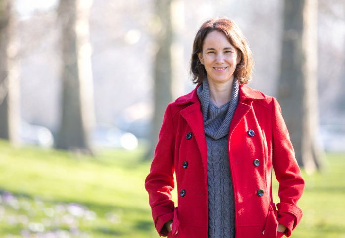 Woman in red coat smiles at camera in green/natural setting