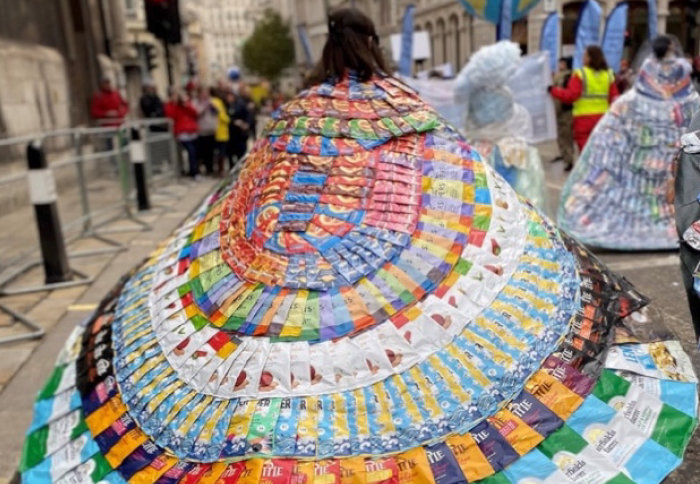 The crisp cloak - a photo of a woman wearing a cape made of crisp packets sewn together into a striped patterned cloak