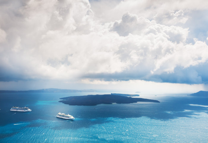 Boats in the ocean near an island below a cloudy sky
