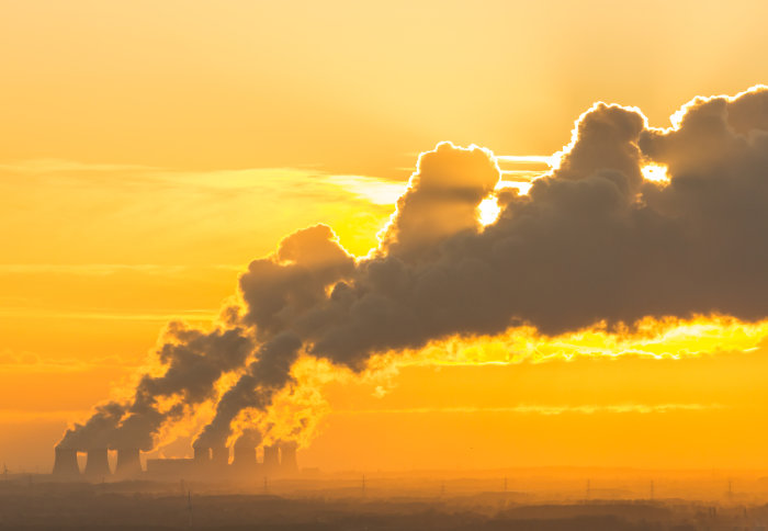 Distant view of a Power Station's cooling towers near Drax in North Yorkshire with the sun setting behind the water vapour trail on a cold winter's night.