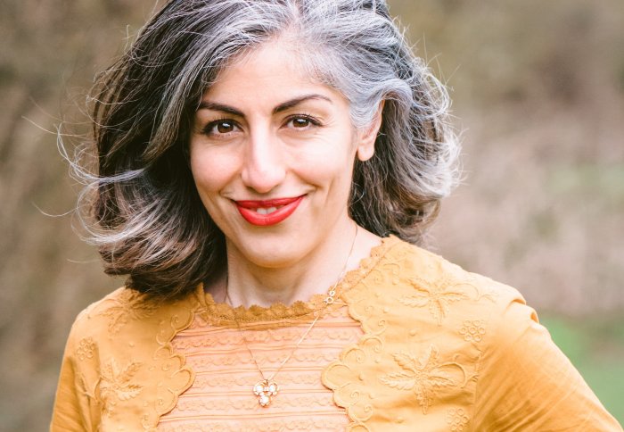 Dr Parry Hashemi standing out doors wearing an orange top and gold necklace