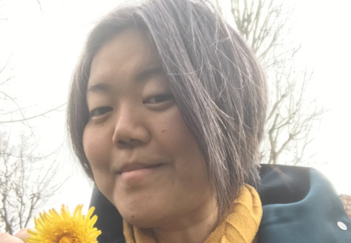 Dr Naomi Nakayama standing outdoors in a blue coat, holding a yellow flower