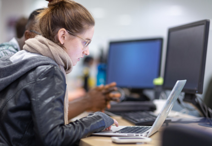 A woman using a laptop with computers in the background