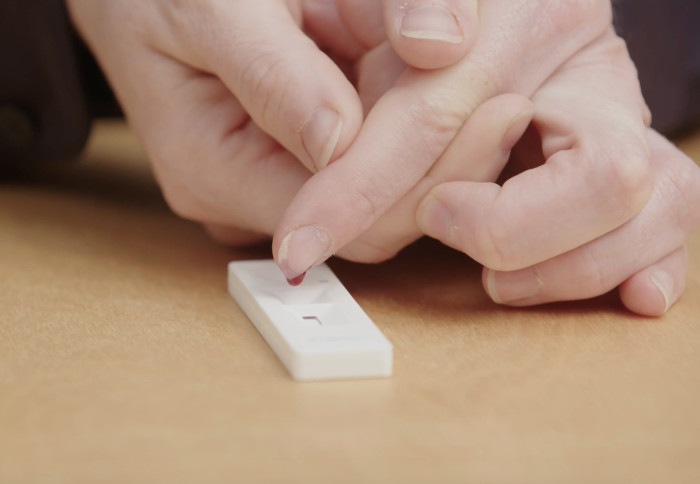 A person placing a drop of blood on a testing stick