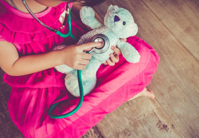 A child holds a stethoscope to a toy teddy bear