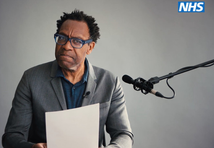 Sir Lenny Henry looking at camera, reading a script next to a microphone
