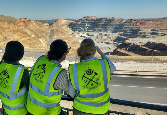 Members of the Department of Earth Science and Engineering at a mine site, with backs to camera in high-vis vest they look out to open cut mine in distance, with blue sky above