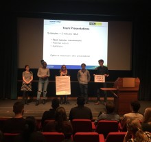 five people stand on a stage giving presentation