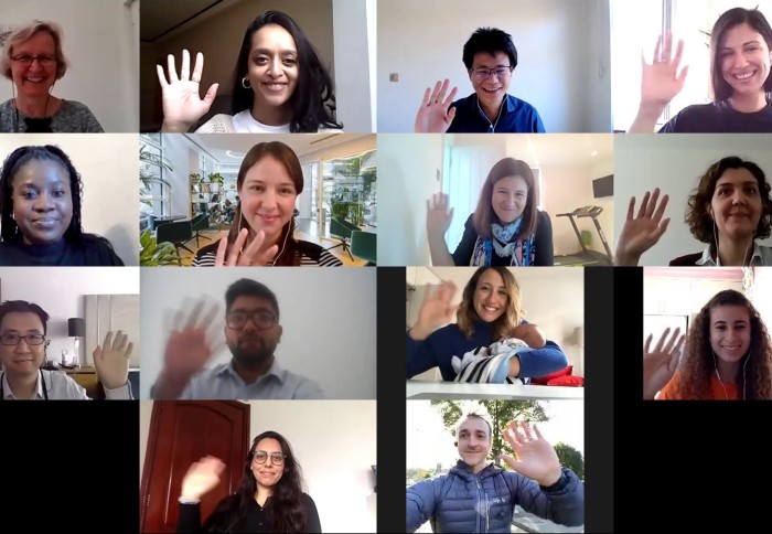 A screenshot of an online meeting with 14 people waving at their cameras from various settings