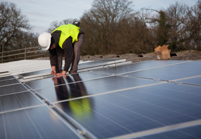 A man in a hardhat installing solar panels on a roof