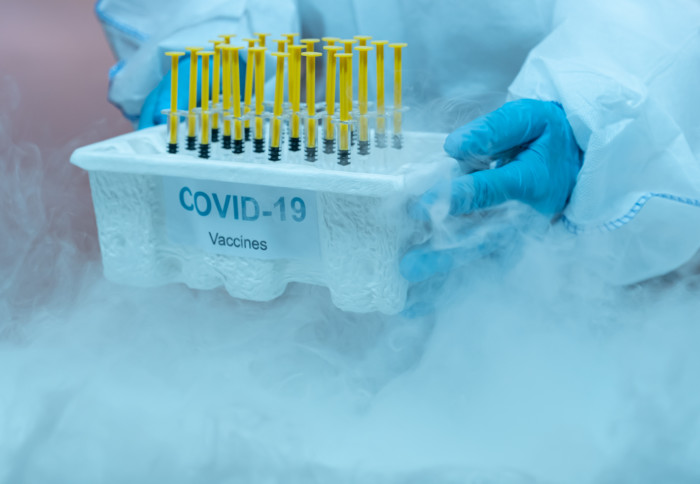 Gloved hands holding a tray of COVID-19 vaccines in a freezer