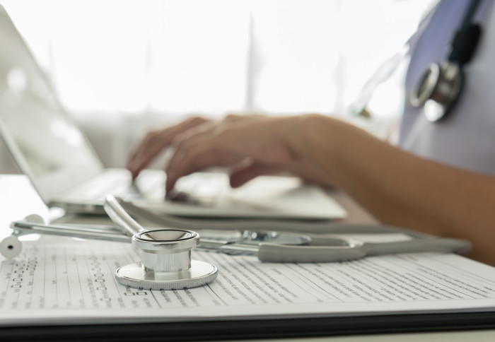 Healthcare staff typing on a laptop with stethoscope on the table