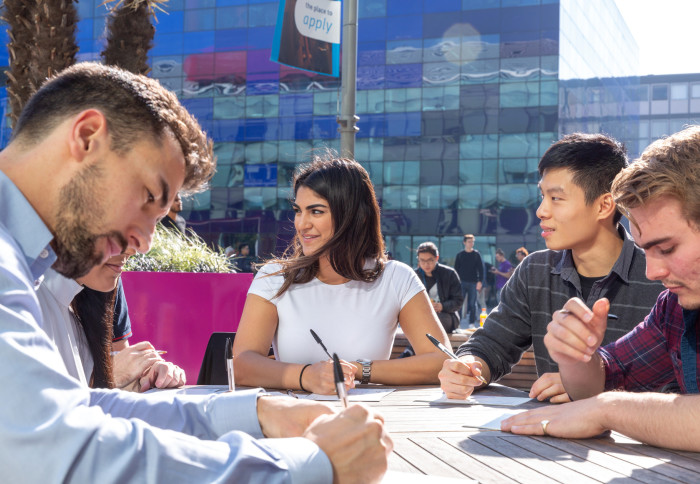 Students on South Kensington campus sit together at a table, writing