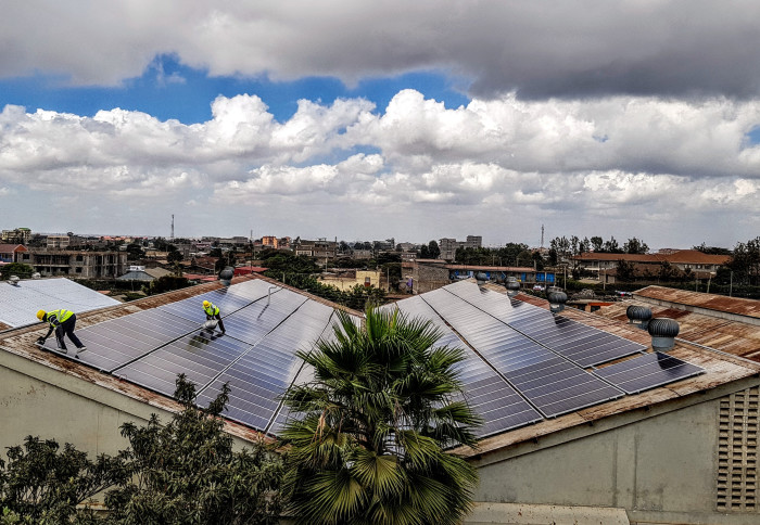 View of a factory roof covered in solar panels, with a town in the background